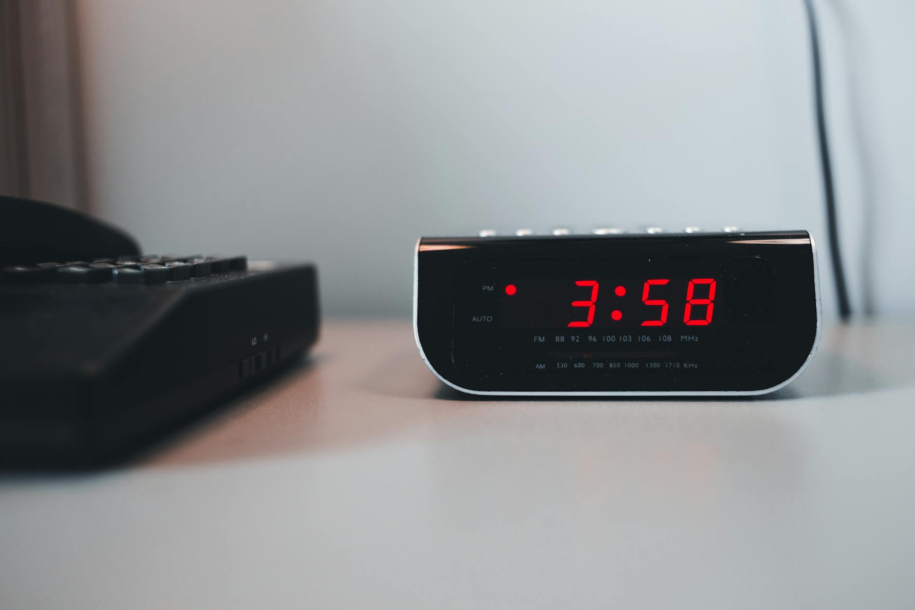 digital alarm clock beside a telephone on a white surface